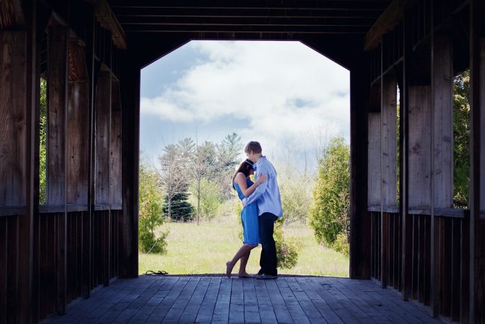 couple poses and is hugging on a covered wooden bridge