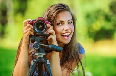 girl smiling behind a camera on a tripod