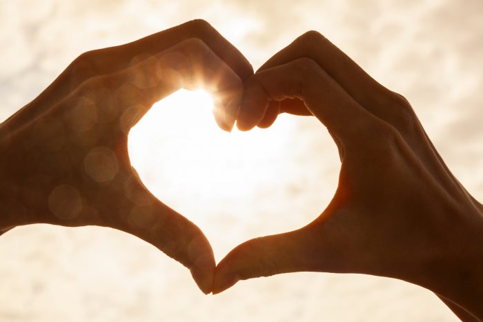 hands forming heart with lens flare in the background